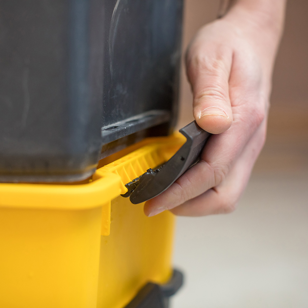 Ręka otwiera zatrzask skrzynki narzędziowej na żółto-czarnej skrzynce.