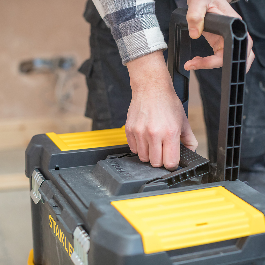Ręka podnosi uchwyt czarno-żółtej skrzynki narzędziowej Stanley.