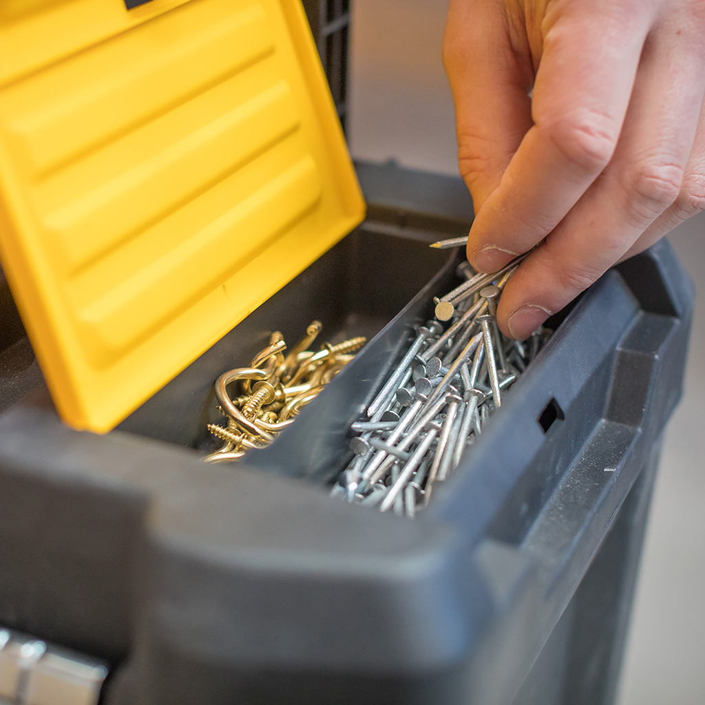 Ręka sięgająca do skrzynki narzędziowej z gwoździami i śrubami w przegródkach.