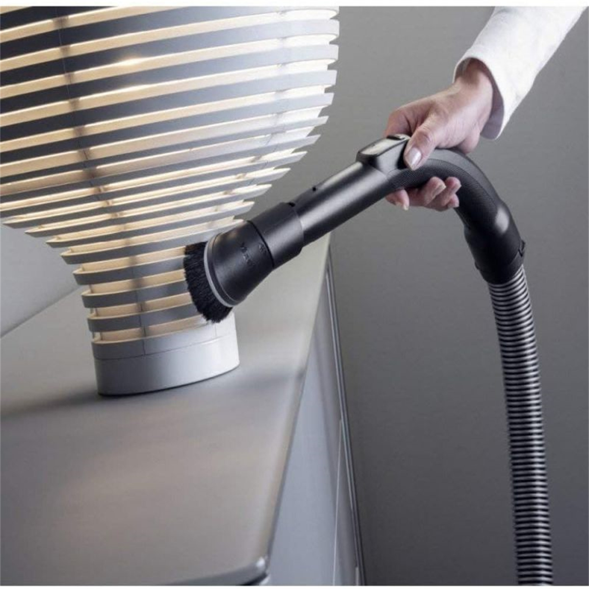 Hand, die einen Staubsaugerbürstenaufsatz in der Nähe einer modernen Lampe hält.
