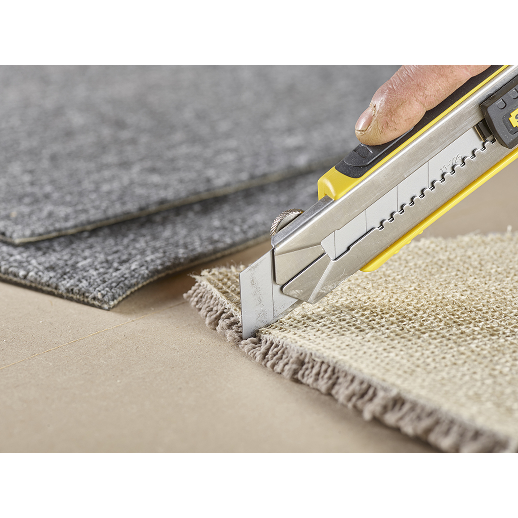 Mano usando un cuchillo Stanley amarillo para cortar alfombra sobre una superficie de madera.