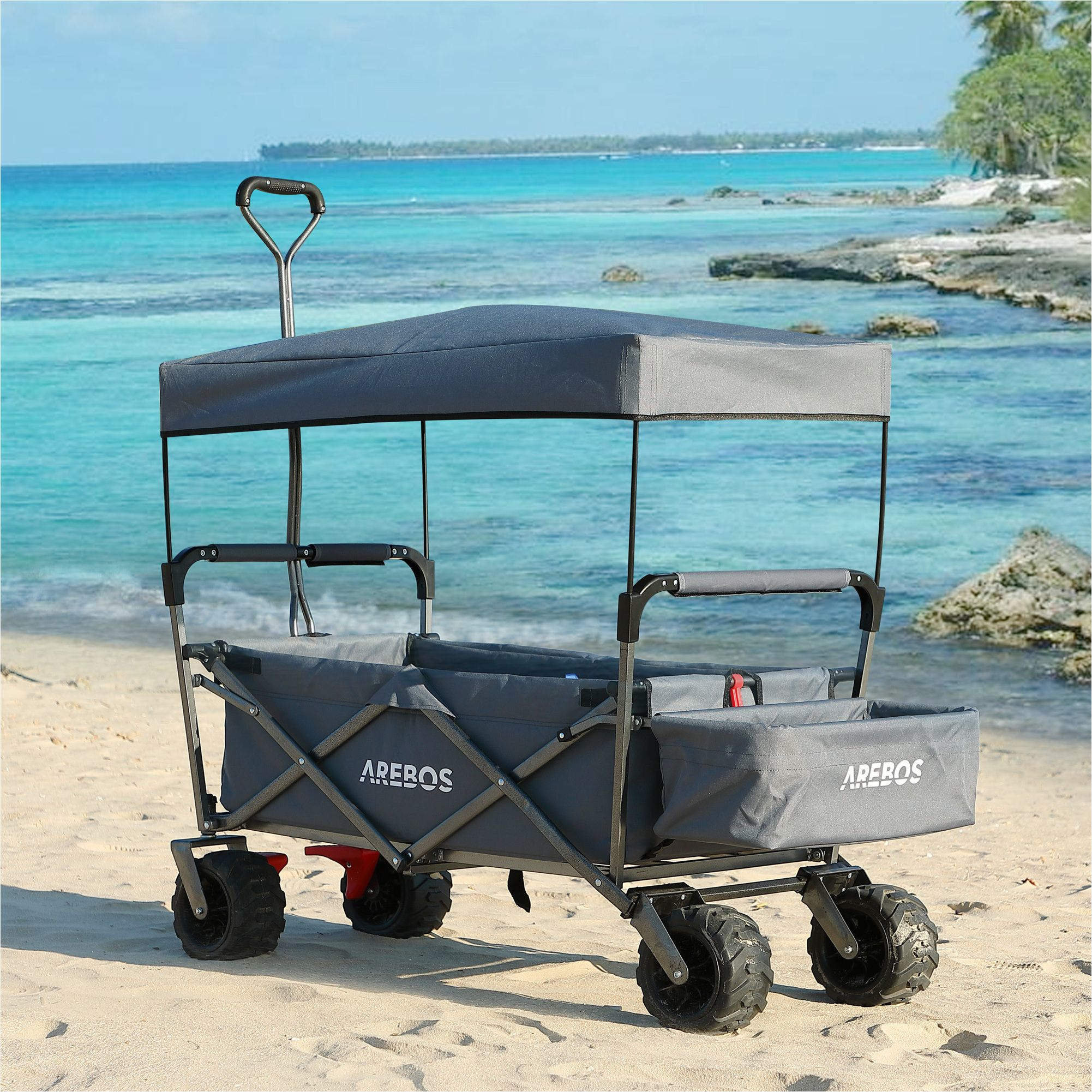 Ein grauer Wagen mit Verdeck an einem Sandstrand mit Meer im Hintergrund.