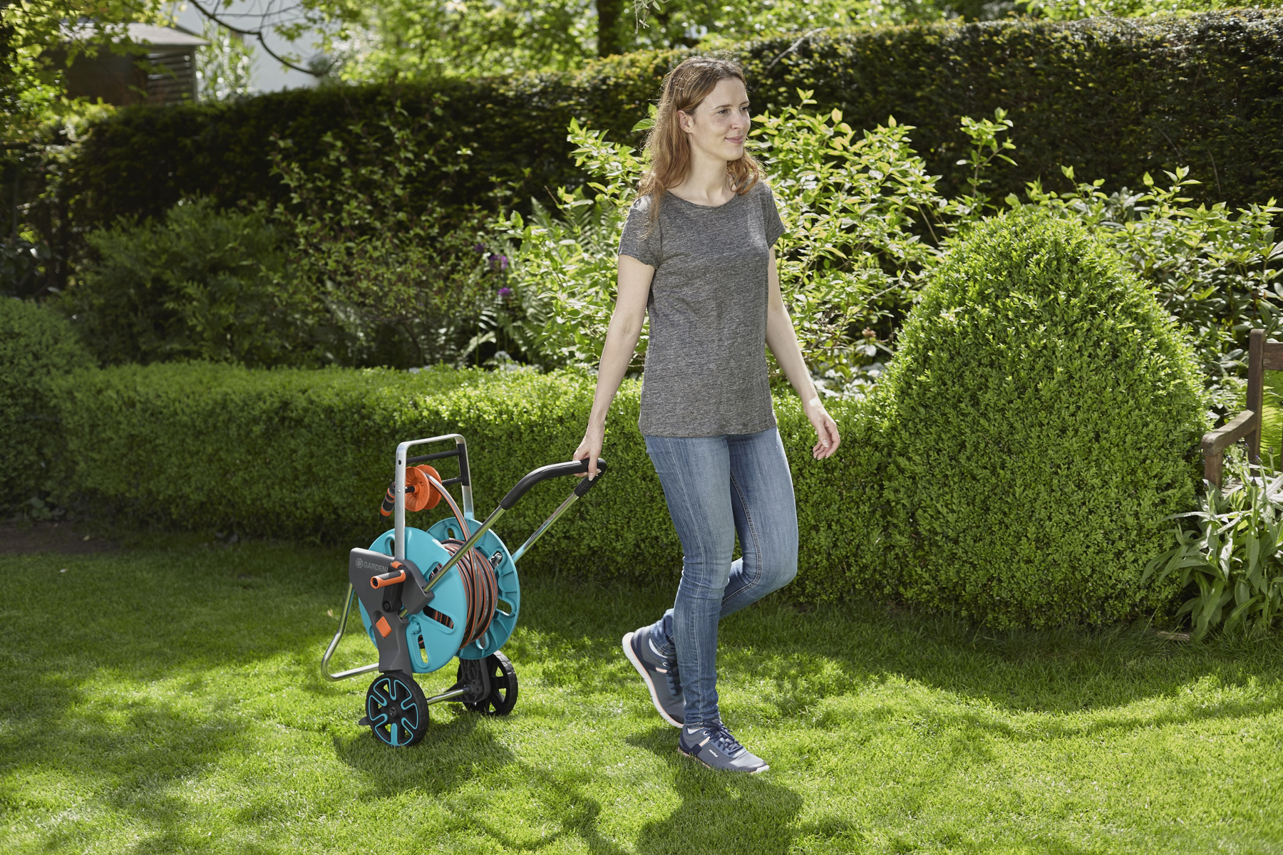 Frau zieht Gartenschlauch-Trommel in sonnigem Garten.