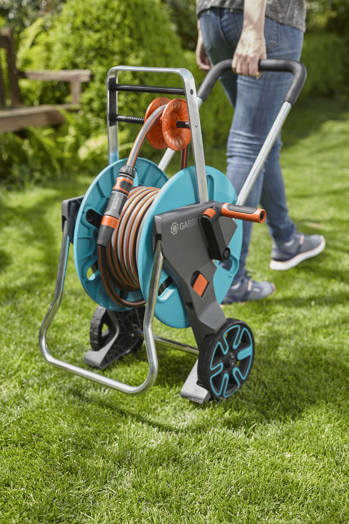 Eine Person zieht eine blau-graue Gartenschlauch-Trommel auf einem grünen Rasen.