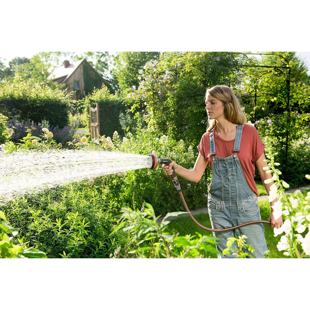 Una mujer usando una manguera, rociando agua en un jardín.