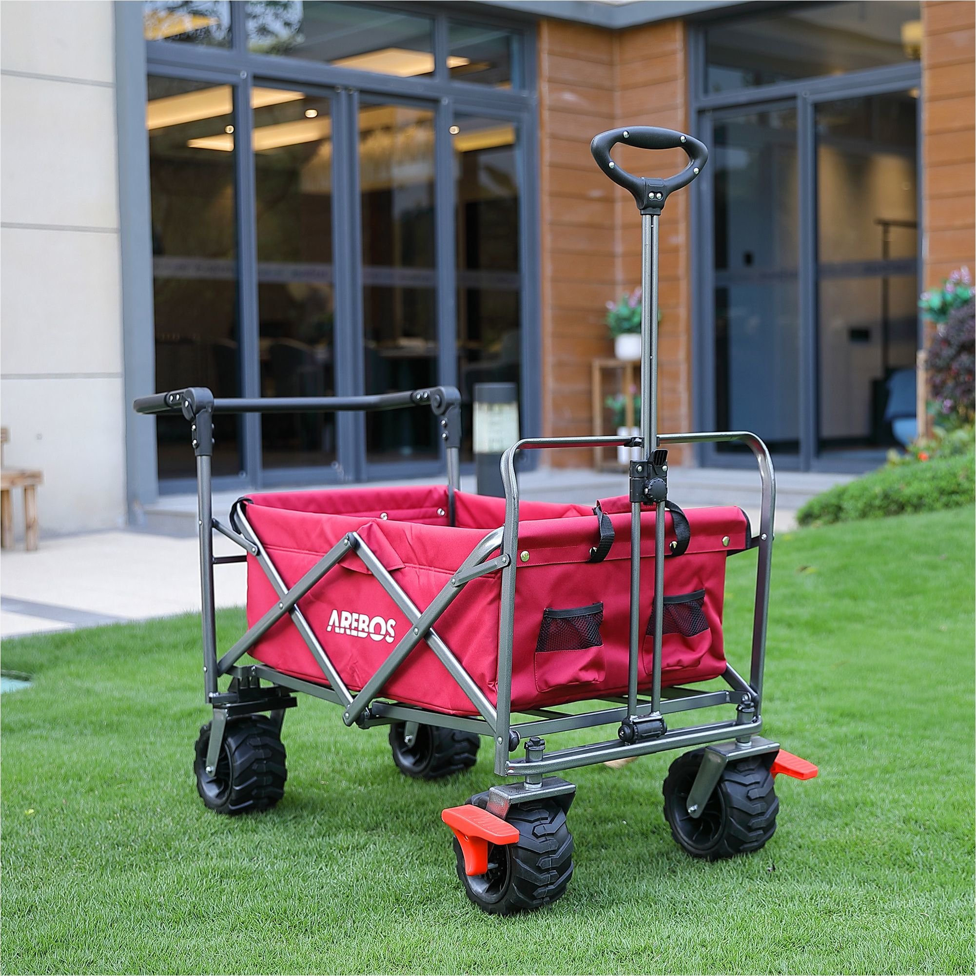 Roter Wagen mit schwarzen Rädern auf grünem Gras, mit Griff und roten Akzenten.