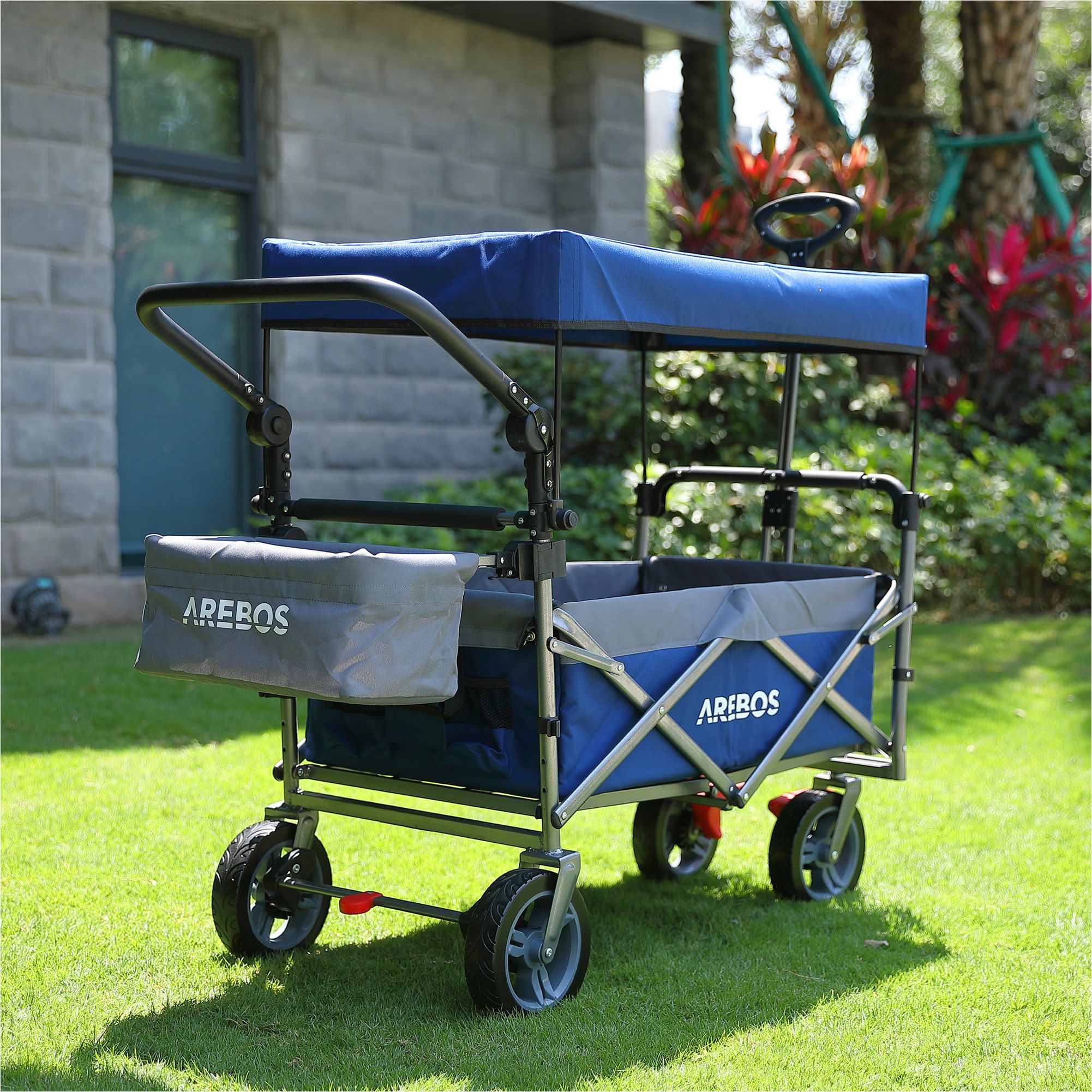 Blau-grauer Wagen mit Verdeck auf Gras. Der Wagen hat große Räder und einen Griff zum Ziehen.