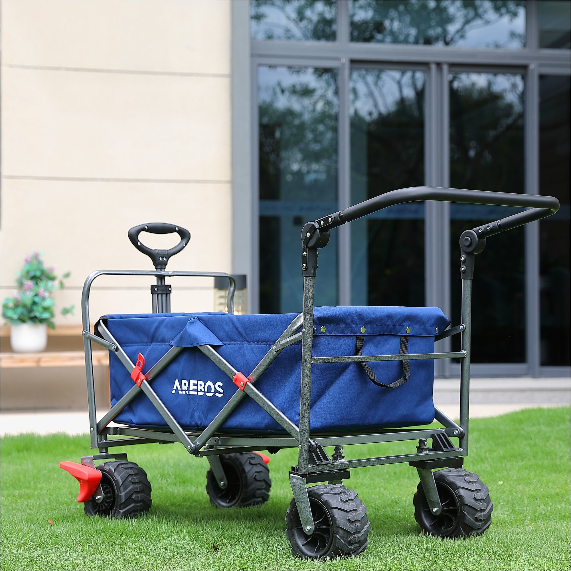 Ein blauer Wagen steht auf Gras. Er hat einen blauen Stoffbehälter, schwarze Reifen und einen Griff.
