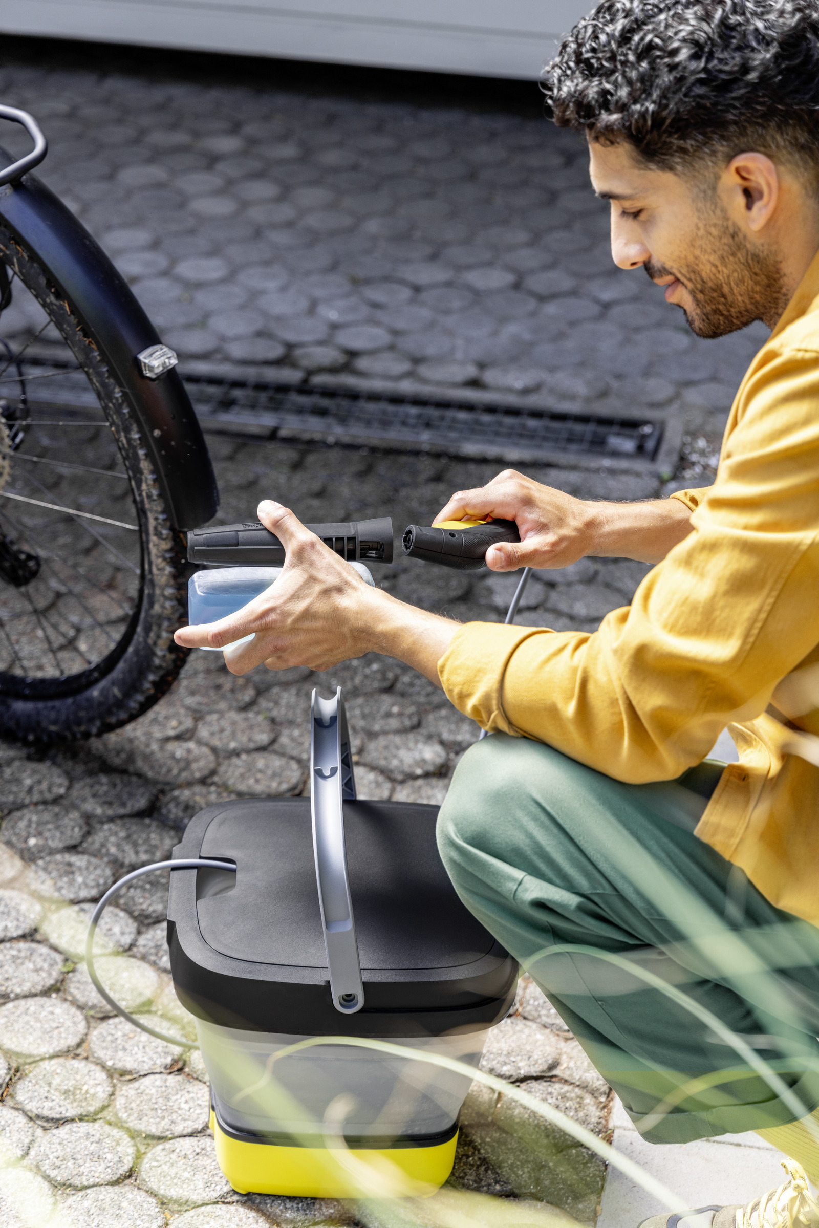 Mężczyzna używający myjki ciśnieniowej Kärcher do czyszczenia roweru na utwardzonej powierzchni.