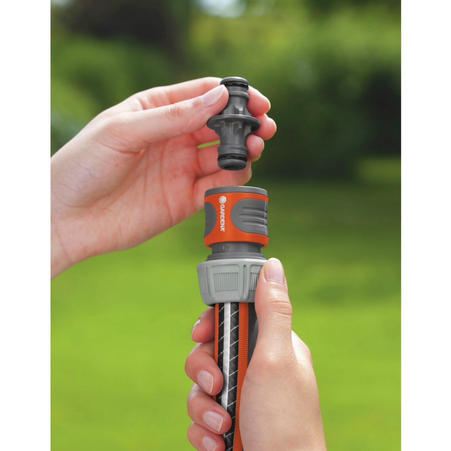 Handen die een slang aansluiten op een GARDENA-connector, groene achtergrond.