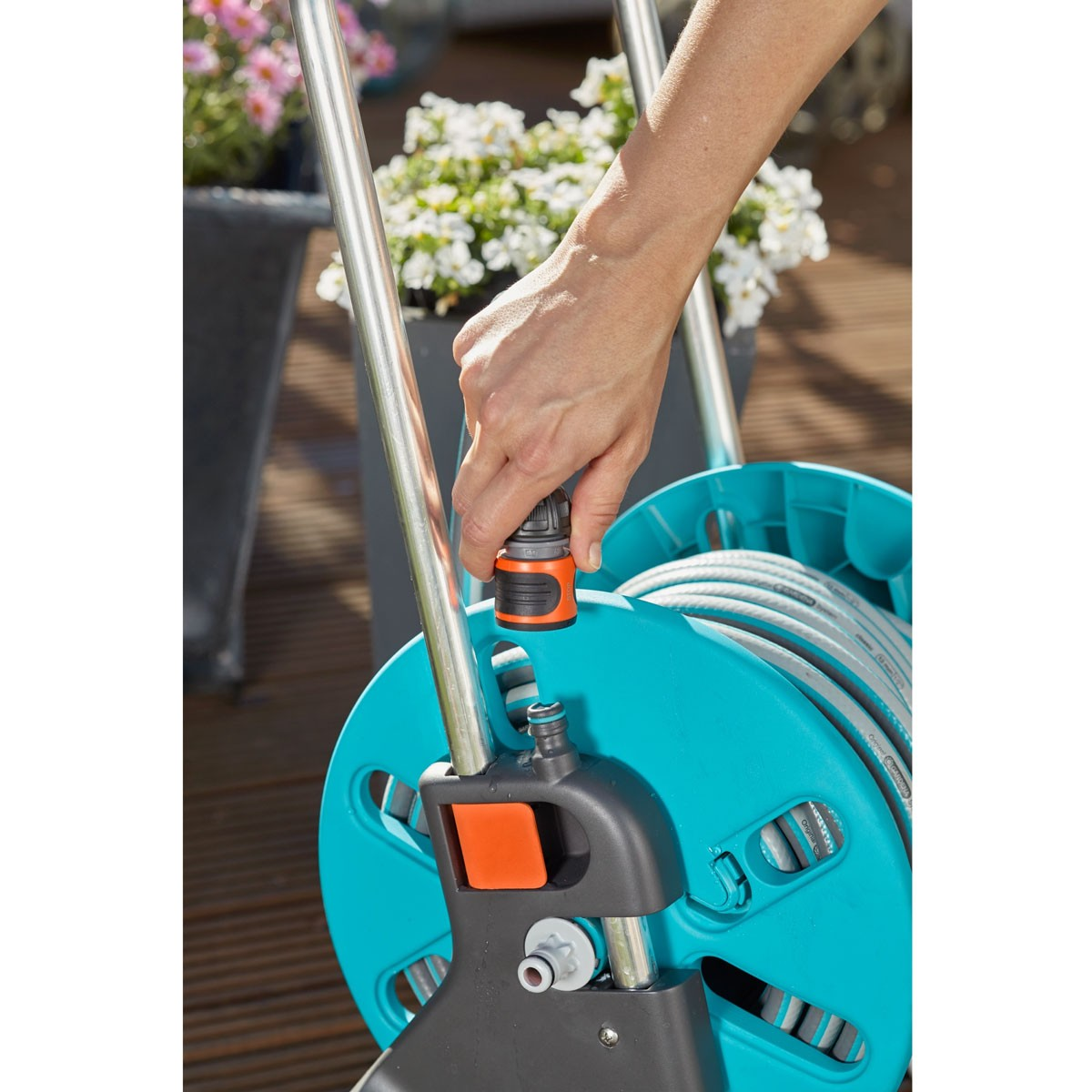 Eine Hand verbindet einen schwarzen und orangenen Schlauchanschluss mit einer blauen Schlauchtrommel mit silbernem Rahmen.