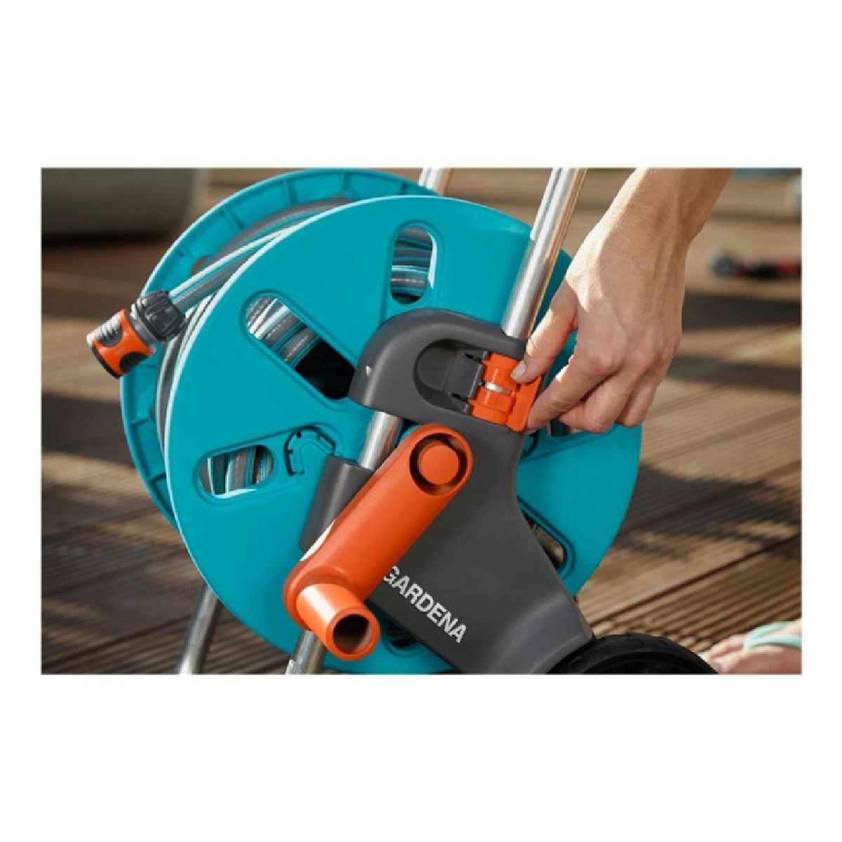 Eine Hand stellt einen orangefarbenen Griff an einer blau-schwarzen Schlauchtrommel auf einem Holzdeck ein.