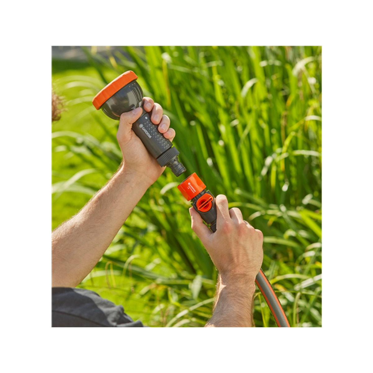 Mani che collegano un ugello nero e arancione per tubo da giardino a un tubo.