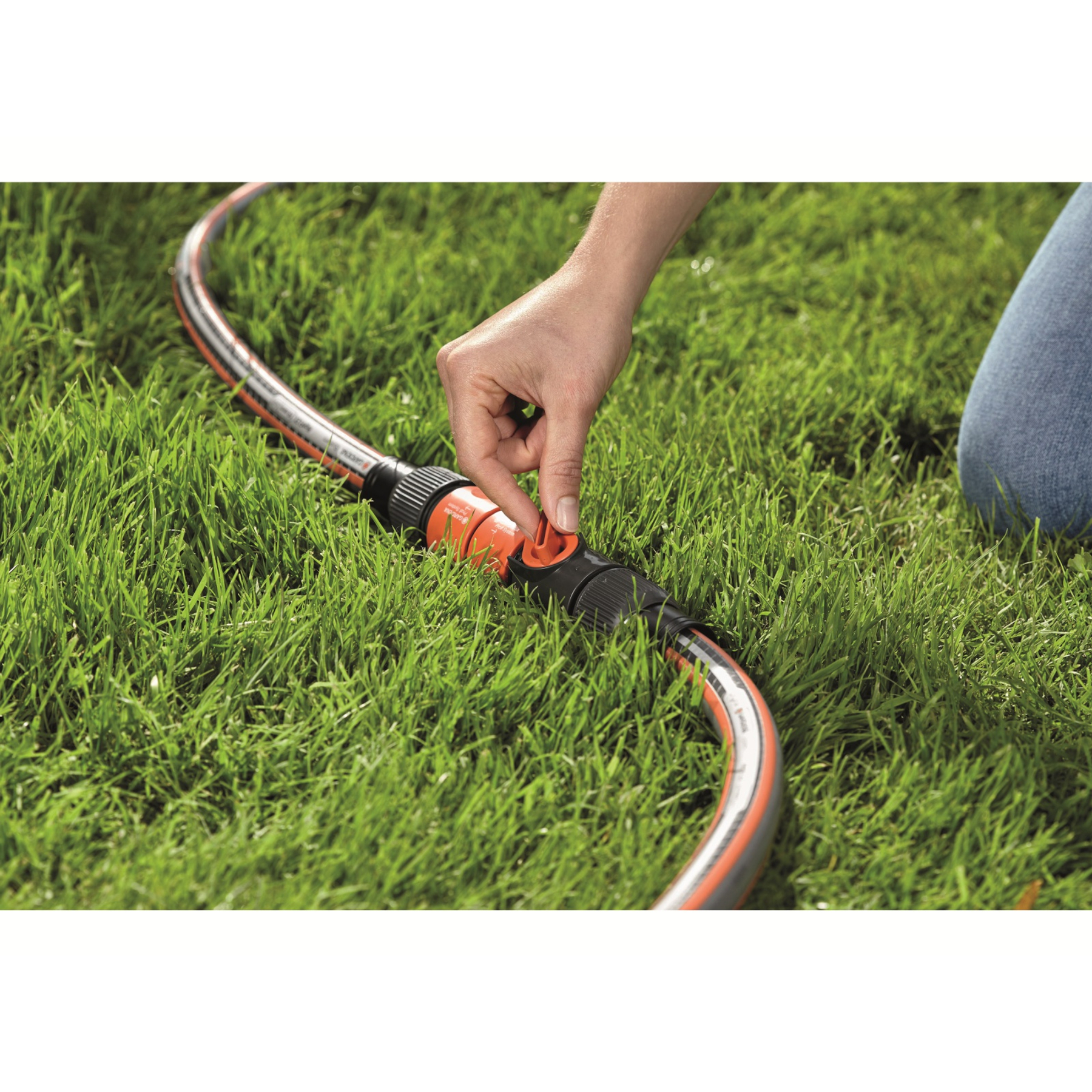 Hand van een persoon die een Gardena slangconnector draait. Groen gras op de achtergrond.