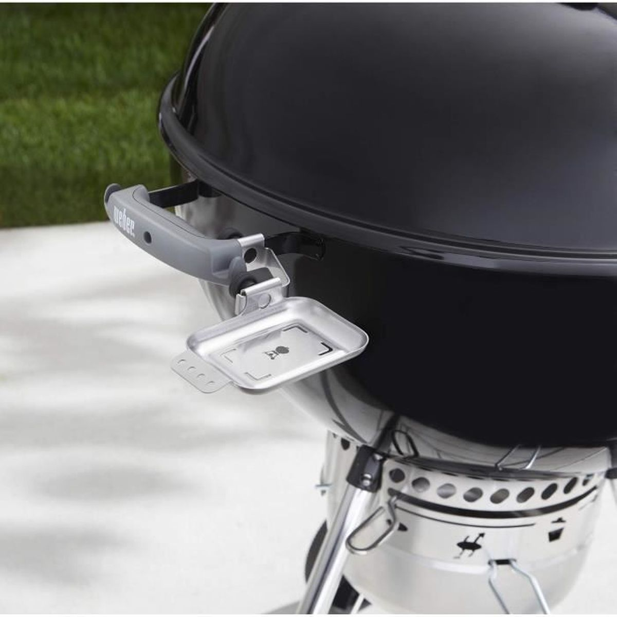 Nahaufnahme eines schwarzen Weber-Grills mit grauem Griff und kleiner Ablage, im Freien.
