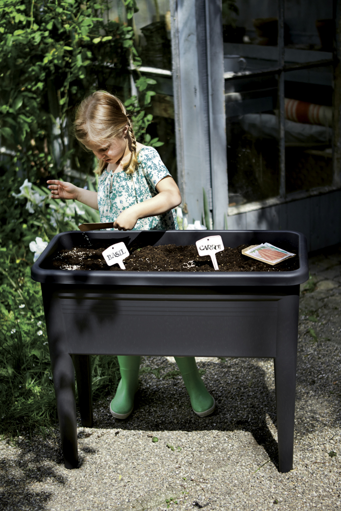 Dziewczyna sadzi w czarnej donicy na nóżkach. Są znaki bazylii i marchwi.