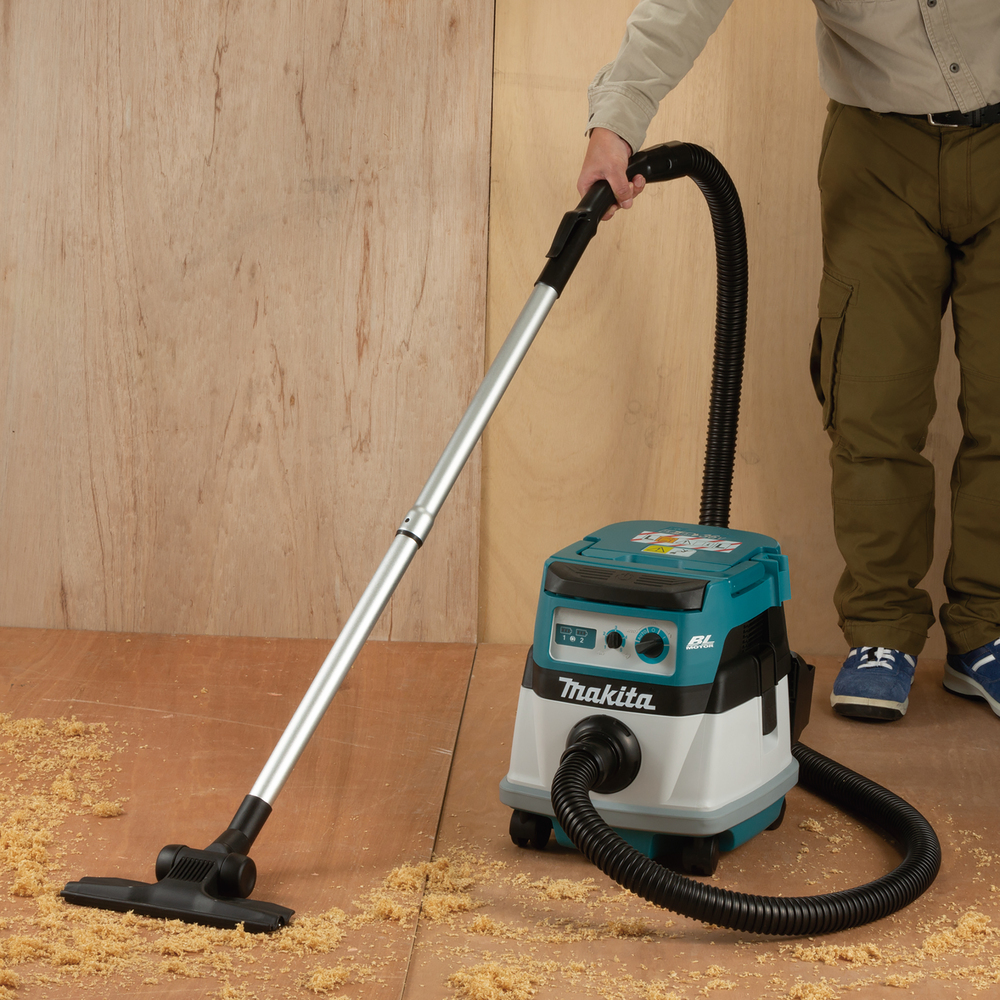 Mann, der einen Makita-Staubsauger auf einem Holzboden benutzt, Sägemehl vorhanden.