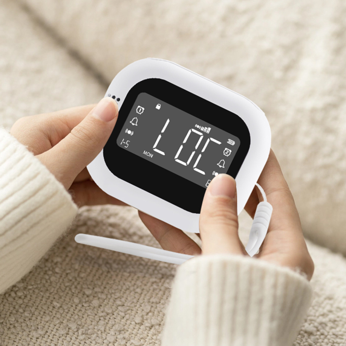 Handen die een witte elektronische babyfoon vasthouden met een digitaal display.