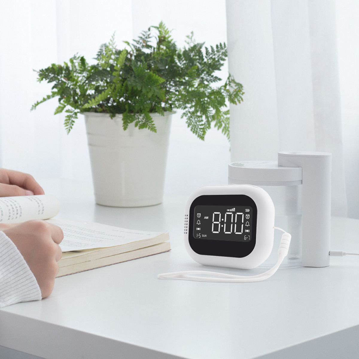 Een witte wekker met 8:00 AM. Een plant en andere items op een witte tafel.