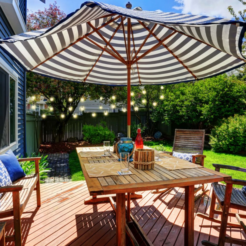 Eethoek buiten met houten tafel, stoelen, gestreepte parasol en lichtsnoeren.