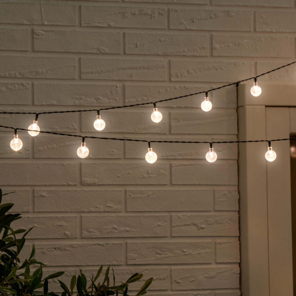 Snoerlampen met heldere bolvormige lampen tegen een witte bakstenen muur. De lichten zijn verlicht.