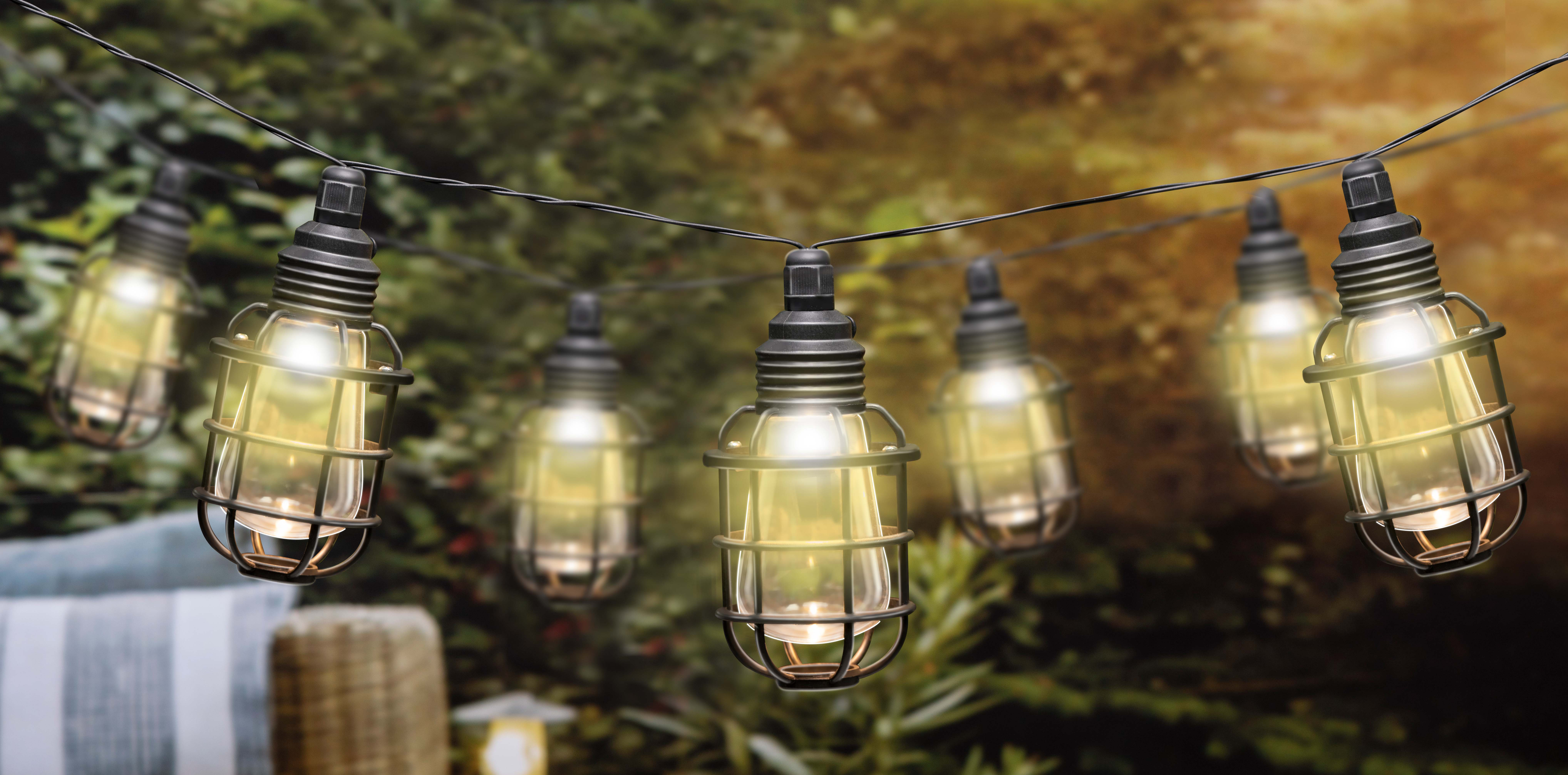Slingerlichtjes met gekooide lampen die in een tuin hangen. De lichten zijn aan.