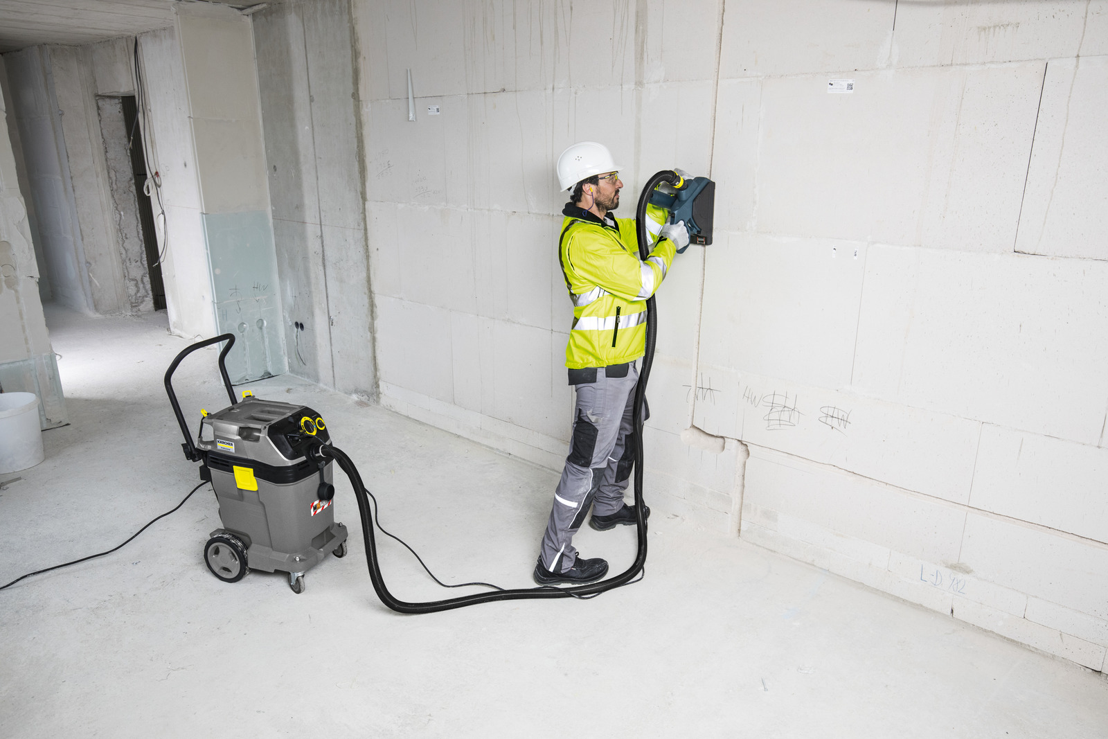 Werknemer snijdt muur met machine aangesloten op stofzuiger. Binnen.