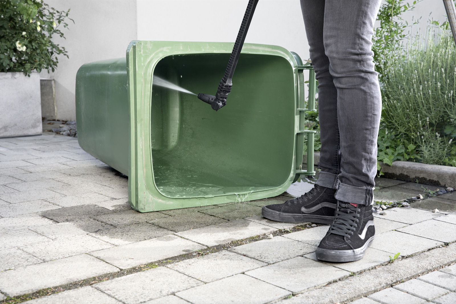 Persona limpiando cubo de basura verde con hidrolavadora. Exterior.