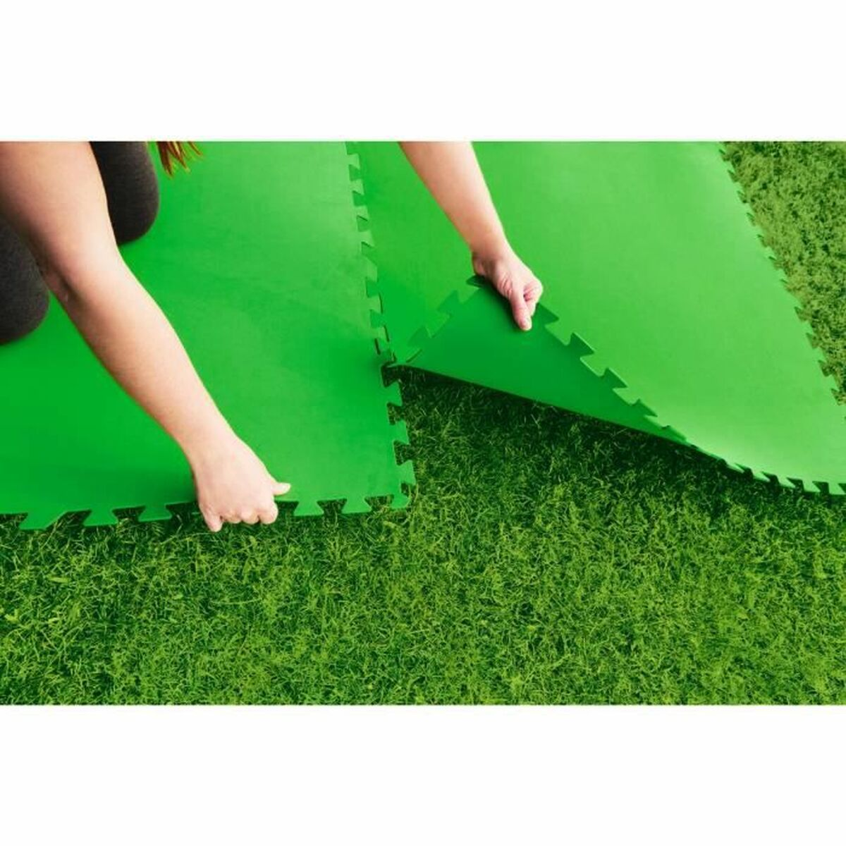 Manos colocando alfombras de espuma verde entrelazadas sobre hierba.