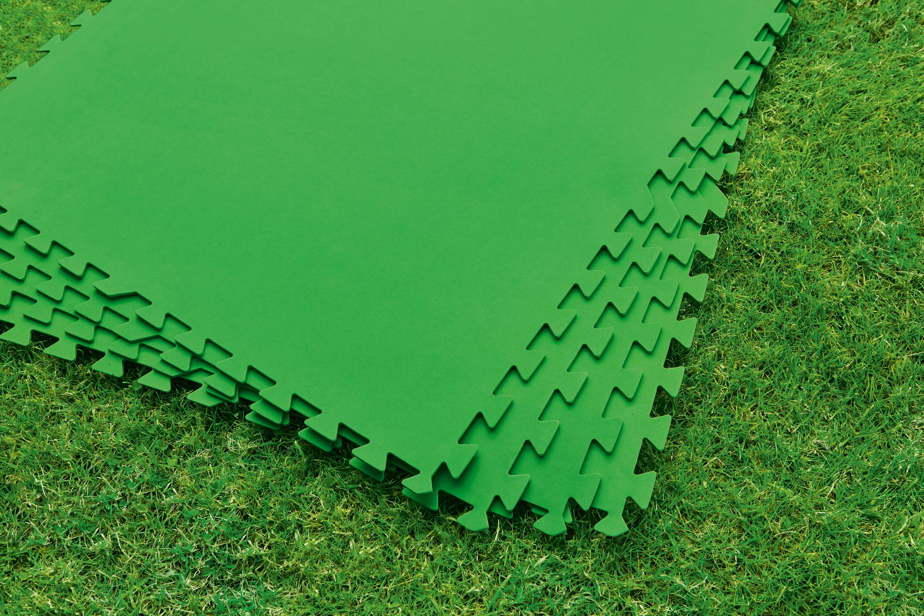 Alfombras de espuma verde entrelazadas sobre hierba, apiladas.