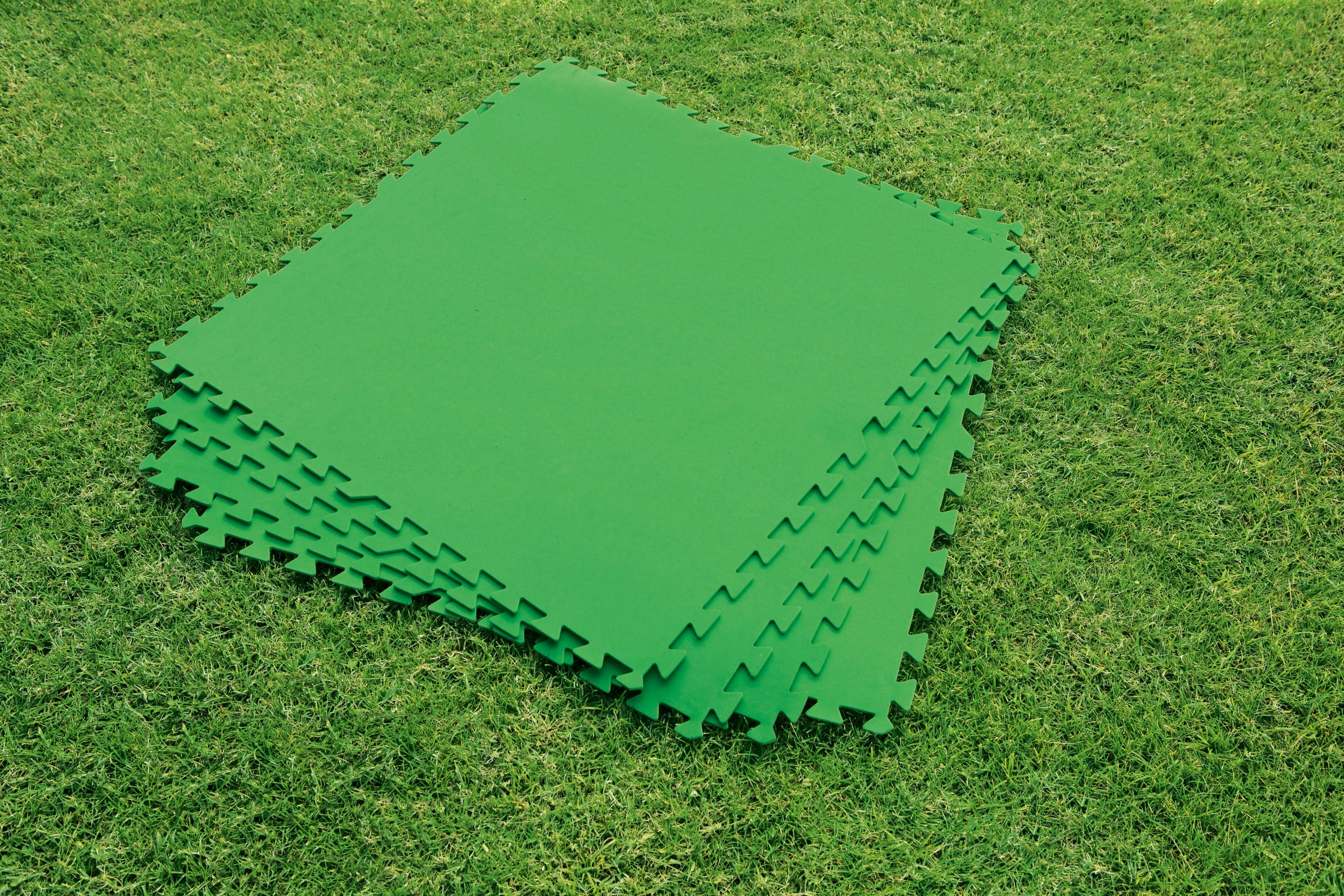 Alfombras de espuma verde entrelazadas sobre hierba, apiladas.