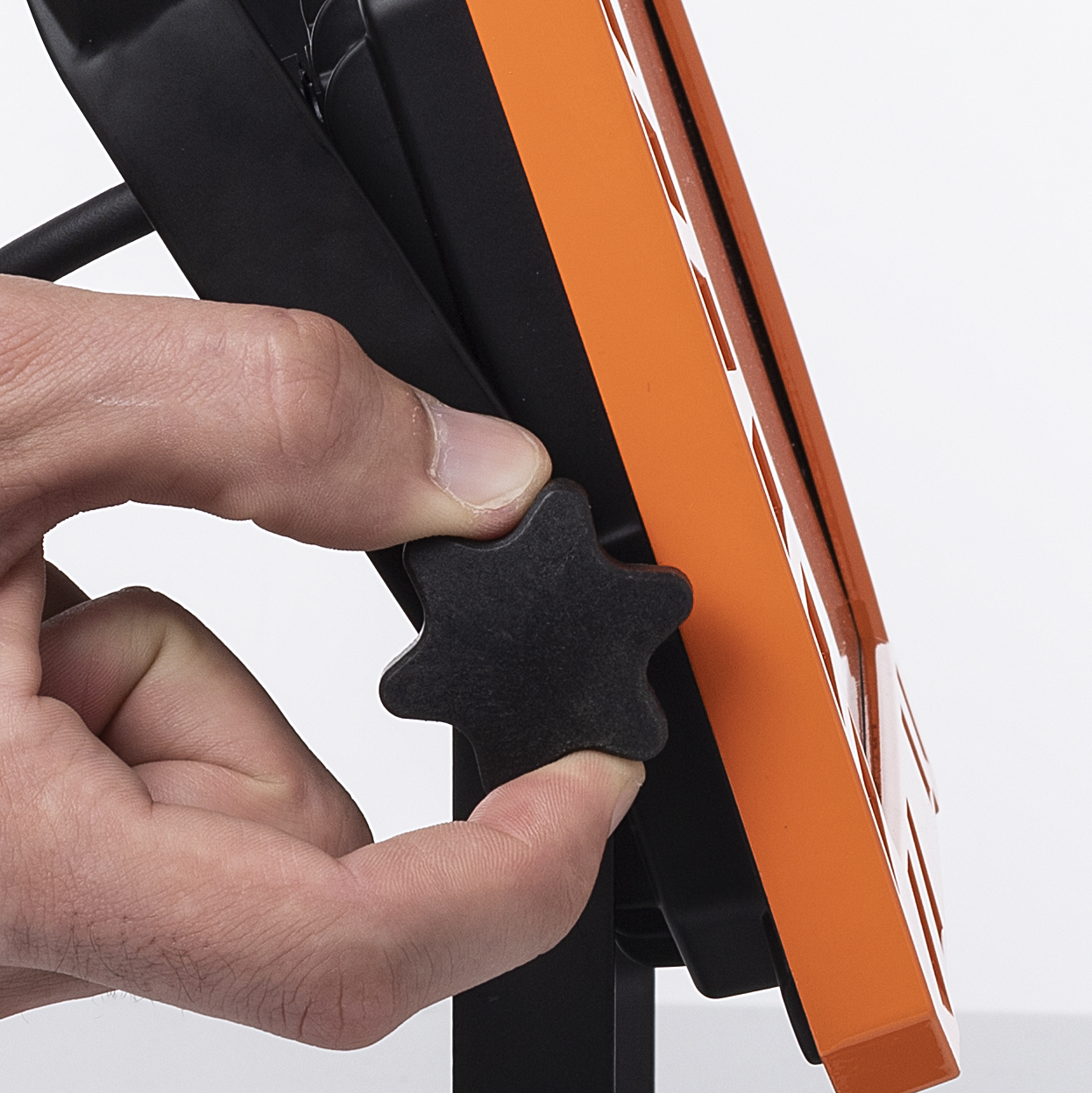 Een hand verstelt de zwarte knop op de werklamp, die oranje en zwart is.
