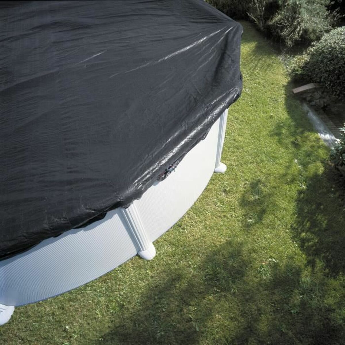 Above ground pool covered in black tarp. Green grass surrounds the pool with a white border.