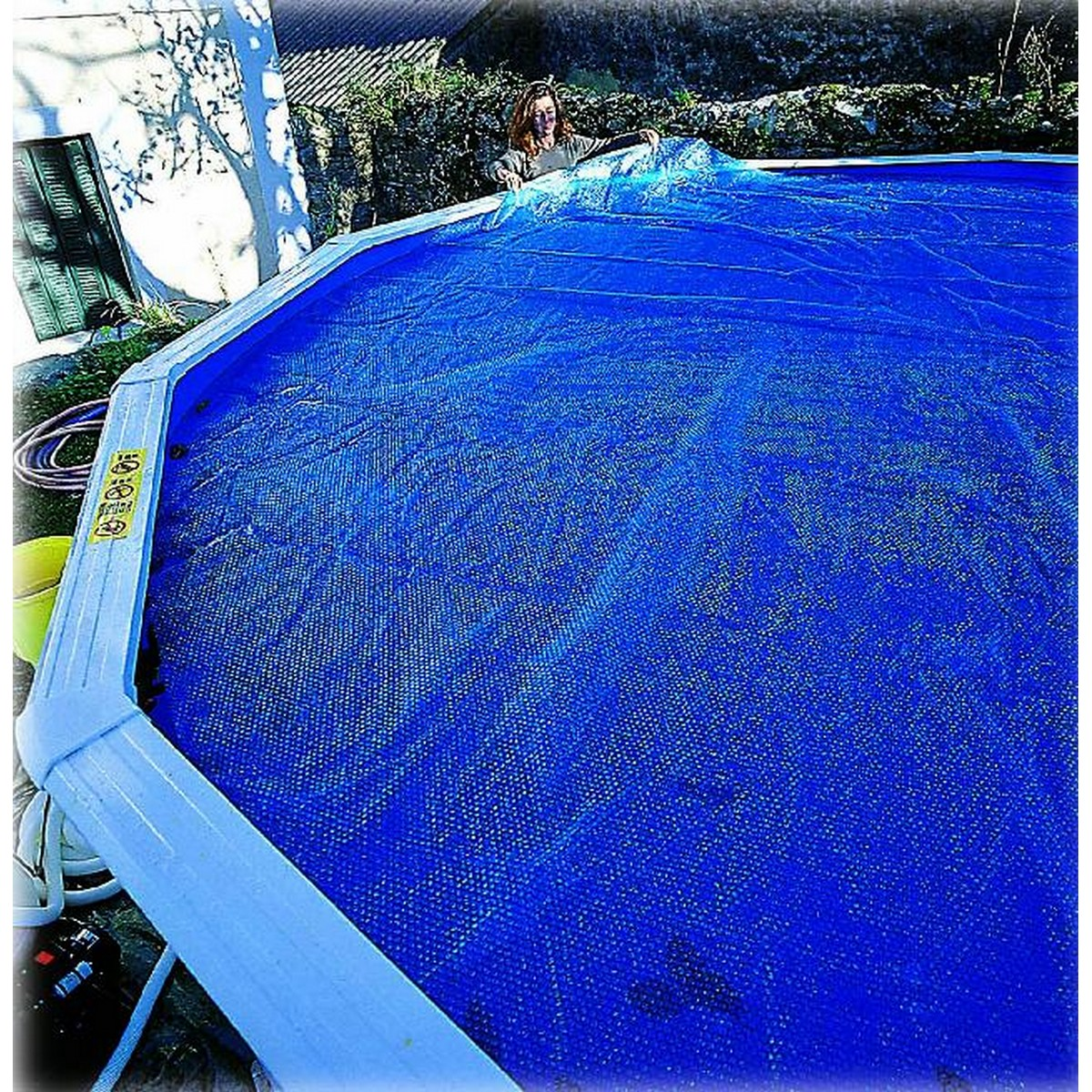 Eine Person legt eine blaue Poolabdeckung auf den Pool. Die Abdeckung hat viele Blasen.
