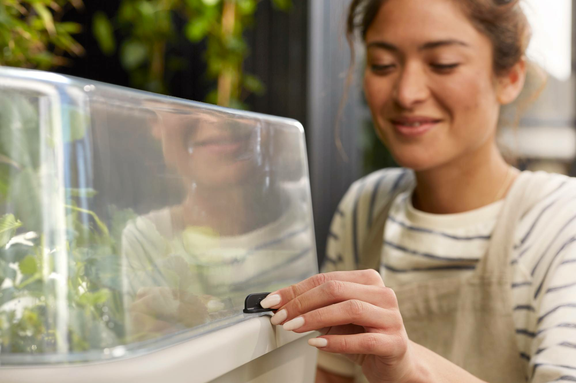 Kobieta regulująca przezroczystą pokrywę na beżowej stacji do przesadzania, uśmiechnięta.