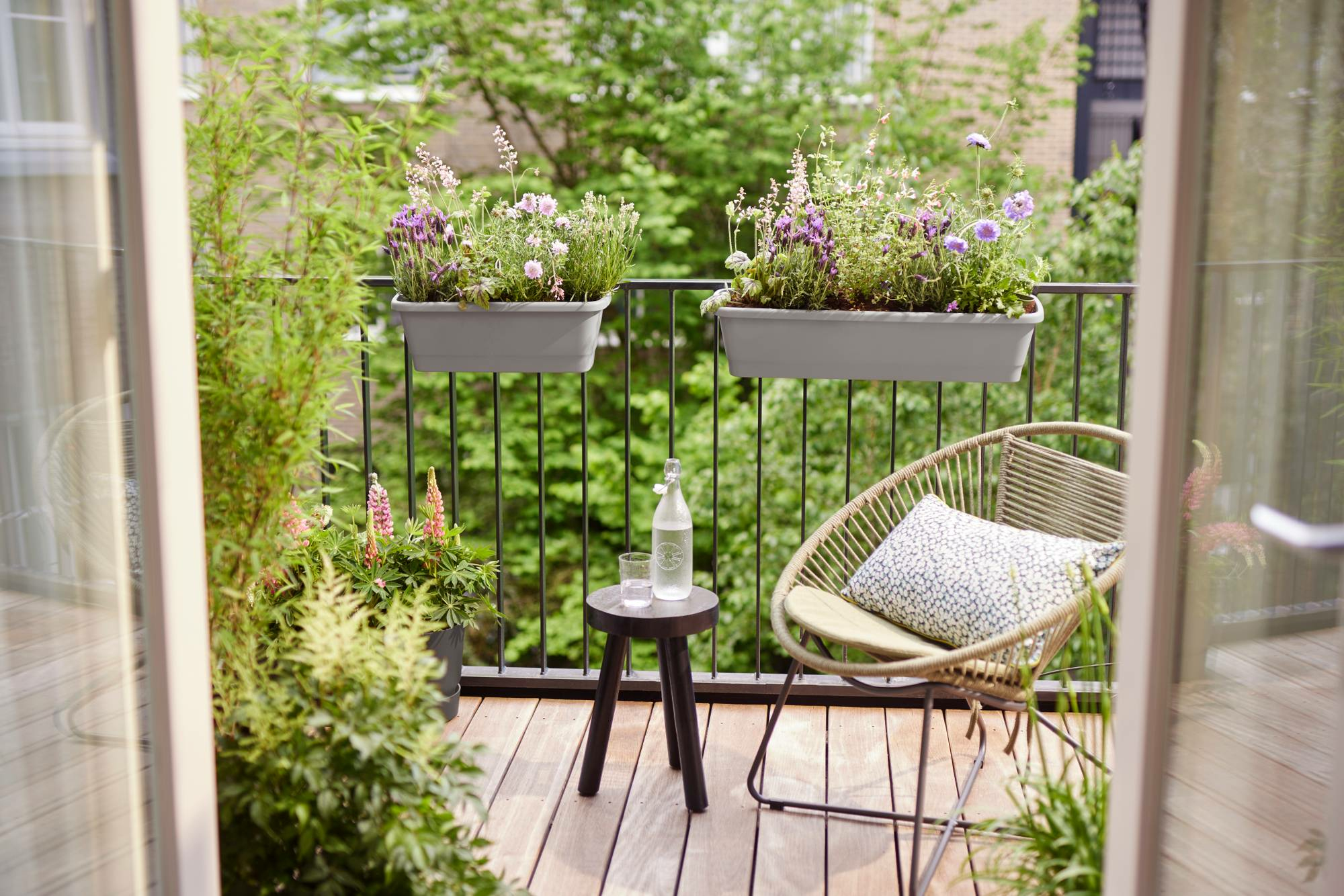 Balkon z roślinami w donicach, krzesłem, stołem i otwartymi drzwiami.