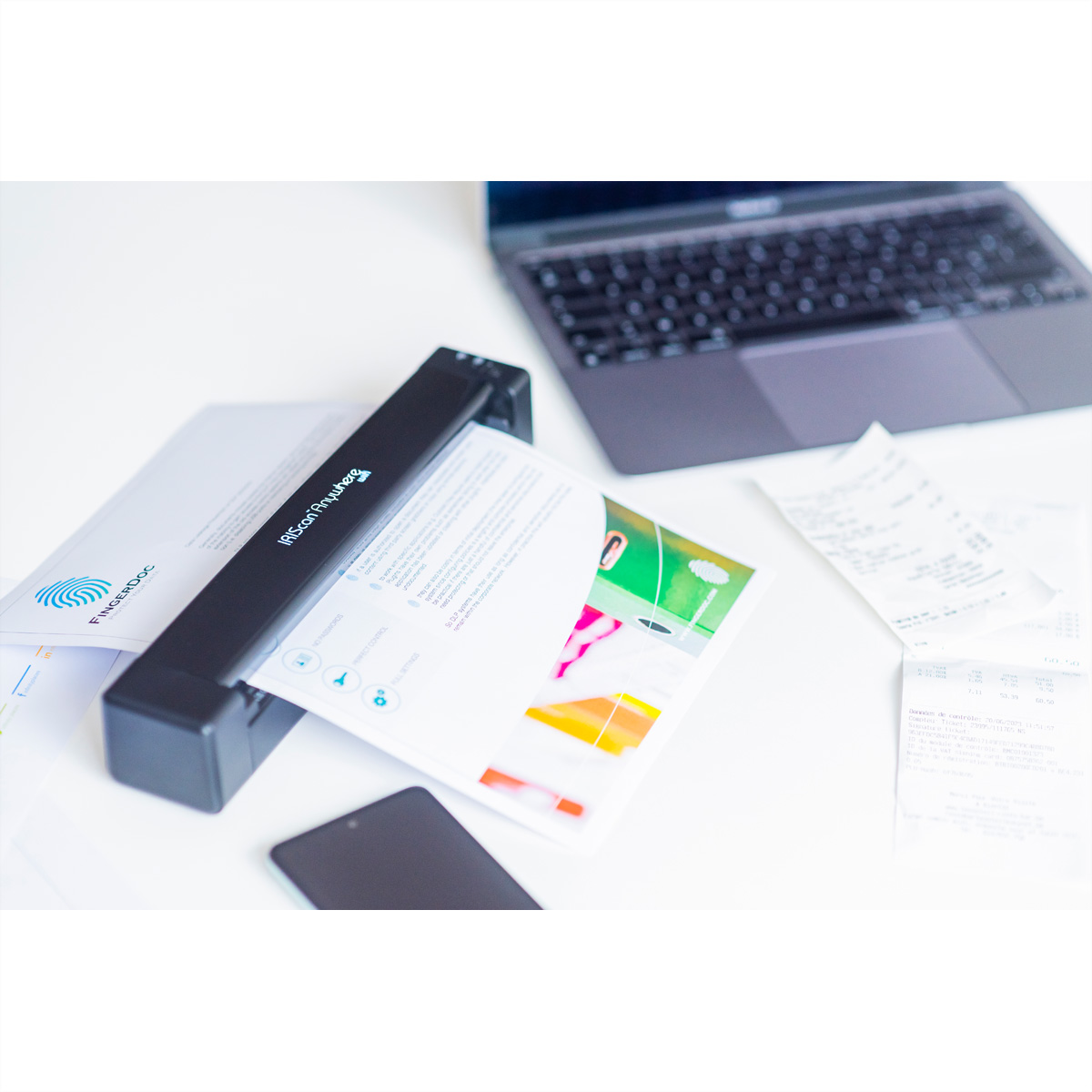 Scanner nero che scansiona un documento. Laptop, telefono e ricevute sulla scrivania bianca.