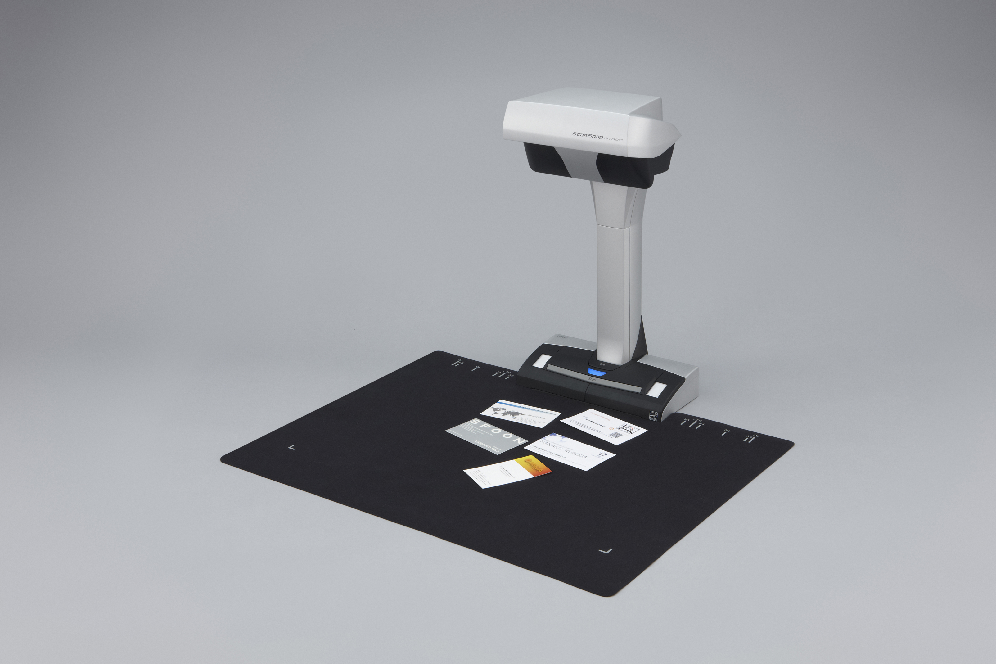 Un escáner cenital con tarjetas de visita sobre una alfombrilla negra. Fondo gris.