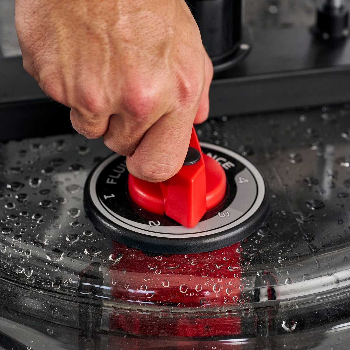 Hand dreht rotes Ventil an einer Maschine. Wassertropfen sichtbar.