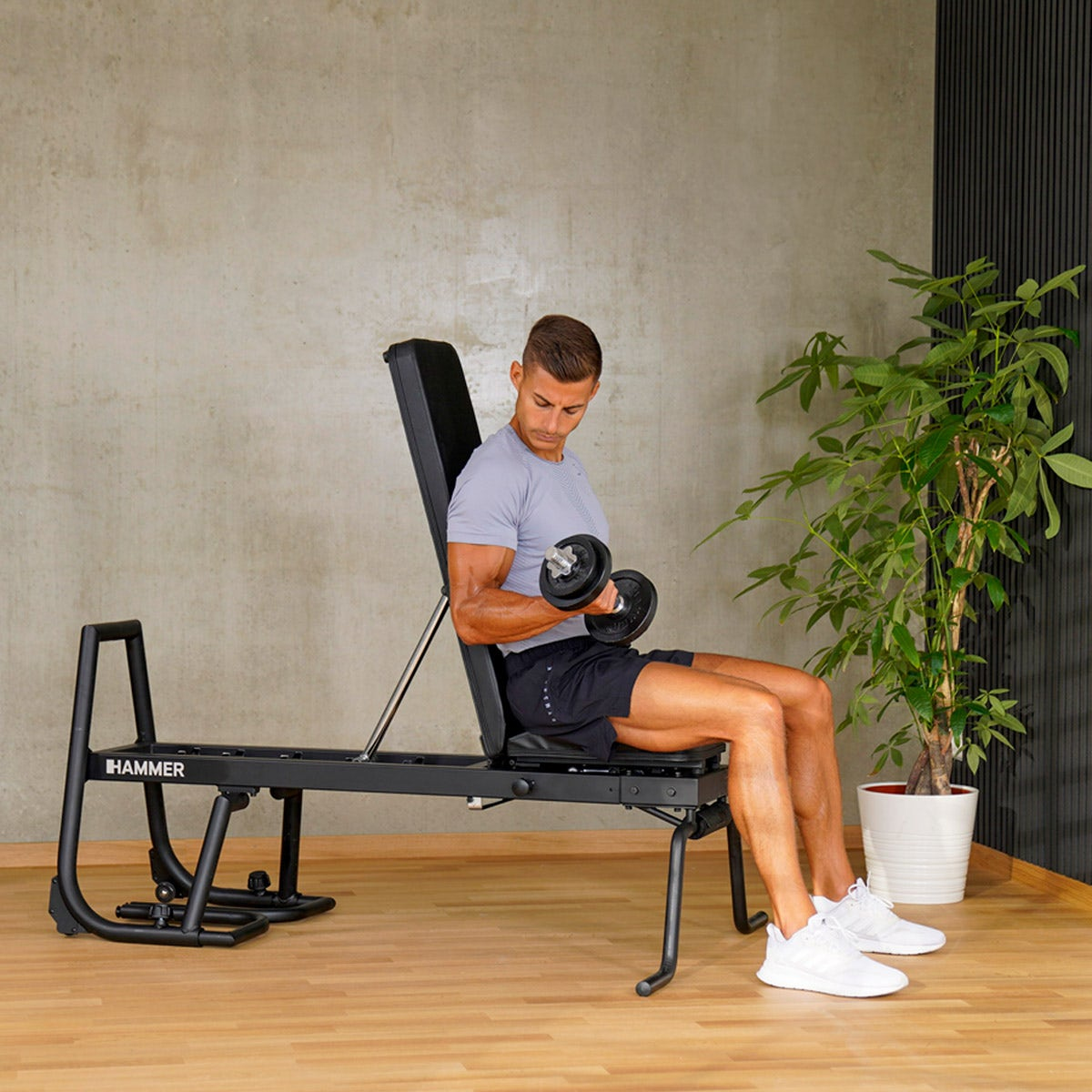 Mann hebt Kurzhantel, sitzend auf schwarzer Hantelbank im Fitnessstudio.