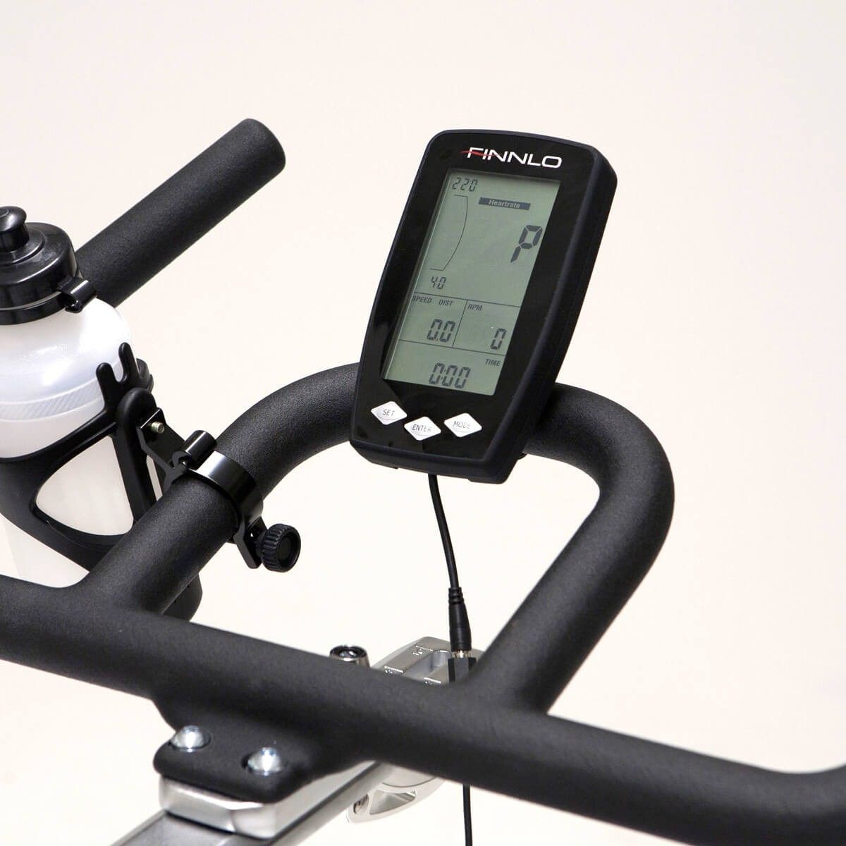 Spinbike-Display mit Geschwindigkeit, RPM, Watt und Zeit. Schwarzer Lenker und Wasserflasche sichtbar.