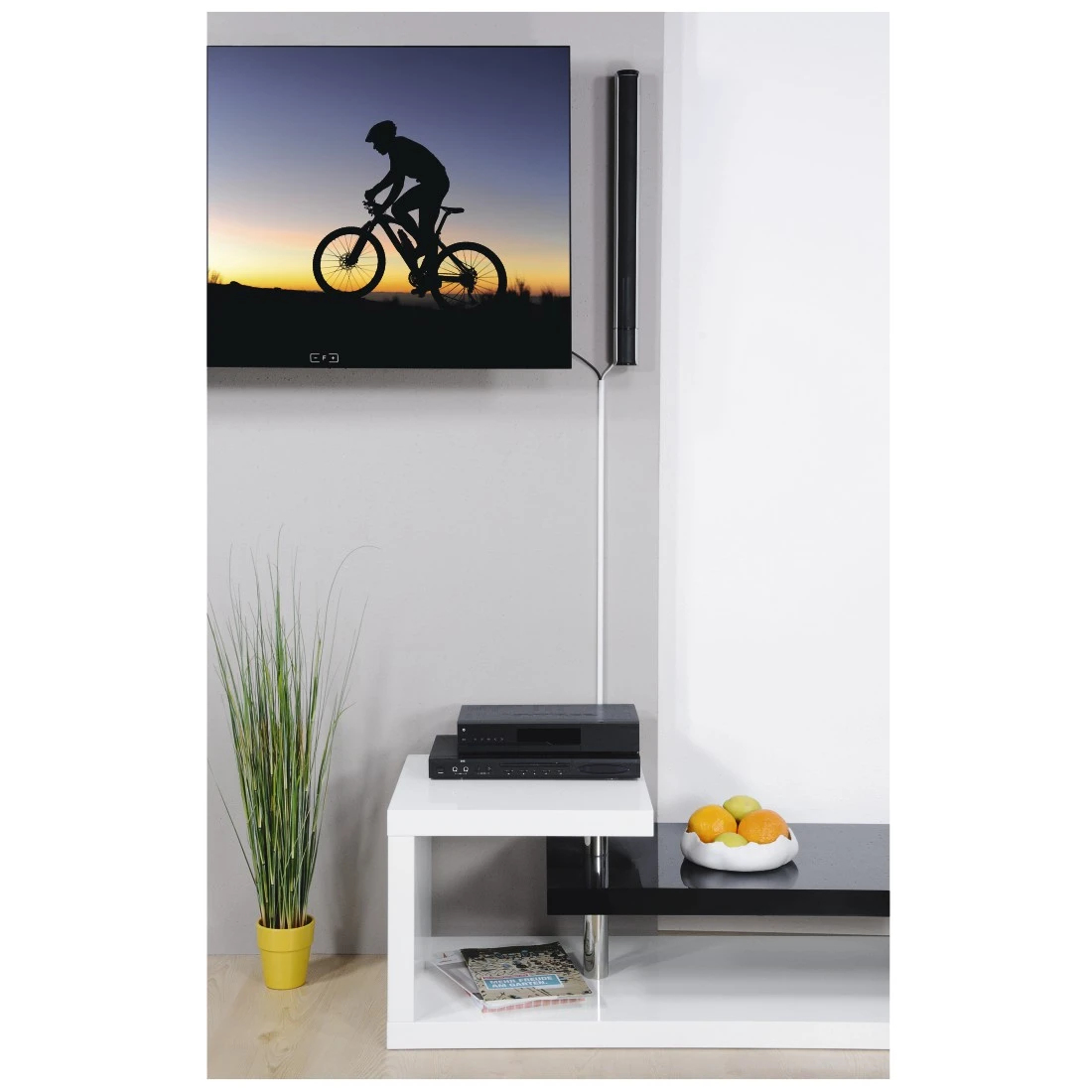 Telewizor z sylwetką rowerzysty. Poniżej biały stół z elektroniką i owocami.