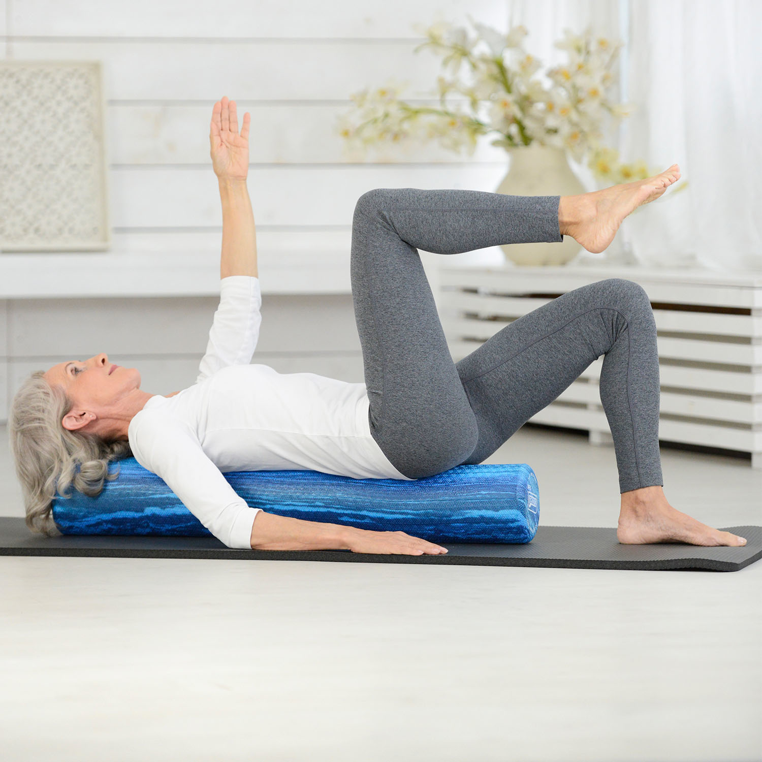 Kobieta ćwicząca na niebieskim wałku piankowym na czarnej macie.