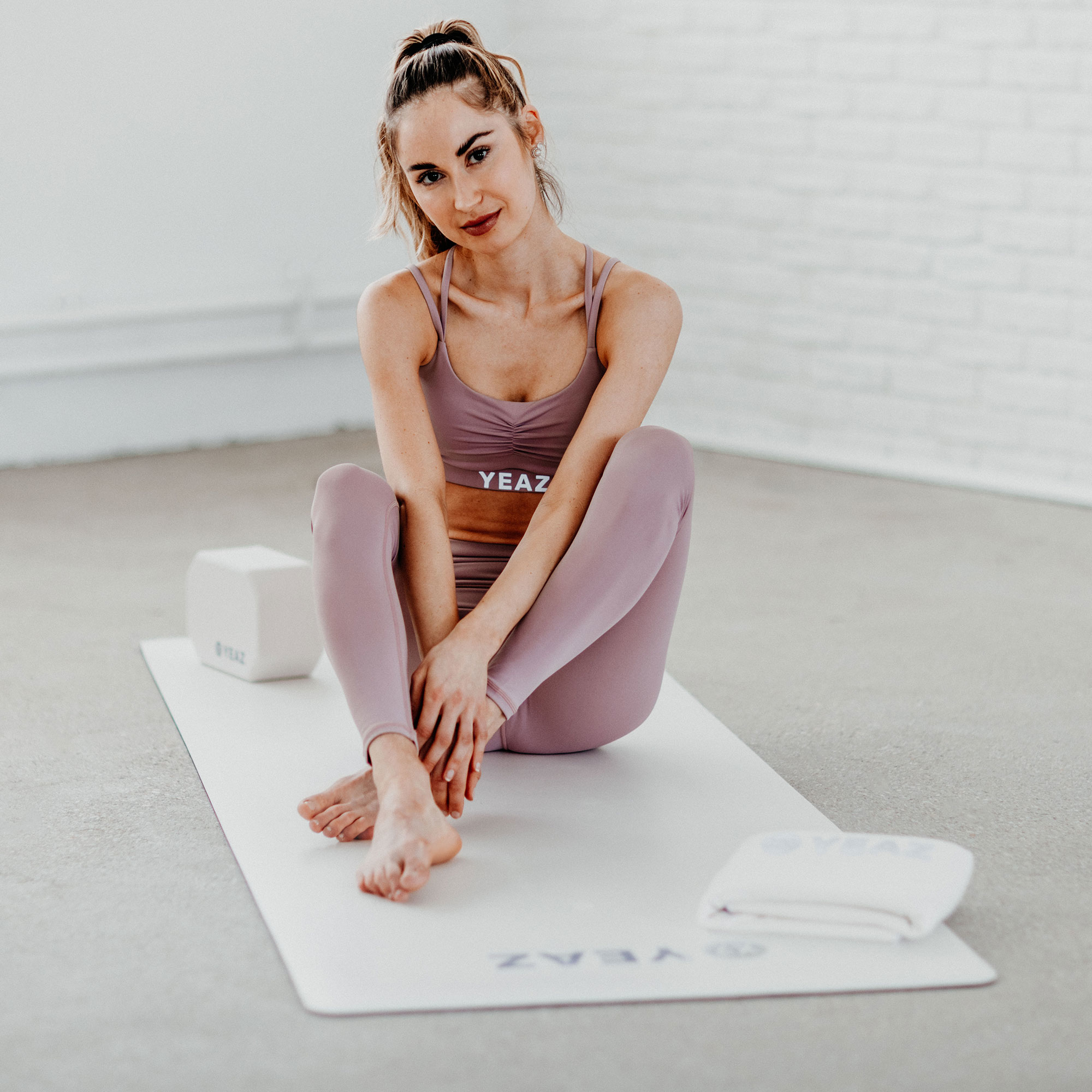 Frau in Yoga-Pose auf Matte, in lila Activewear, mit Blöcken und Handtuch in der Nähe.