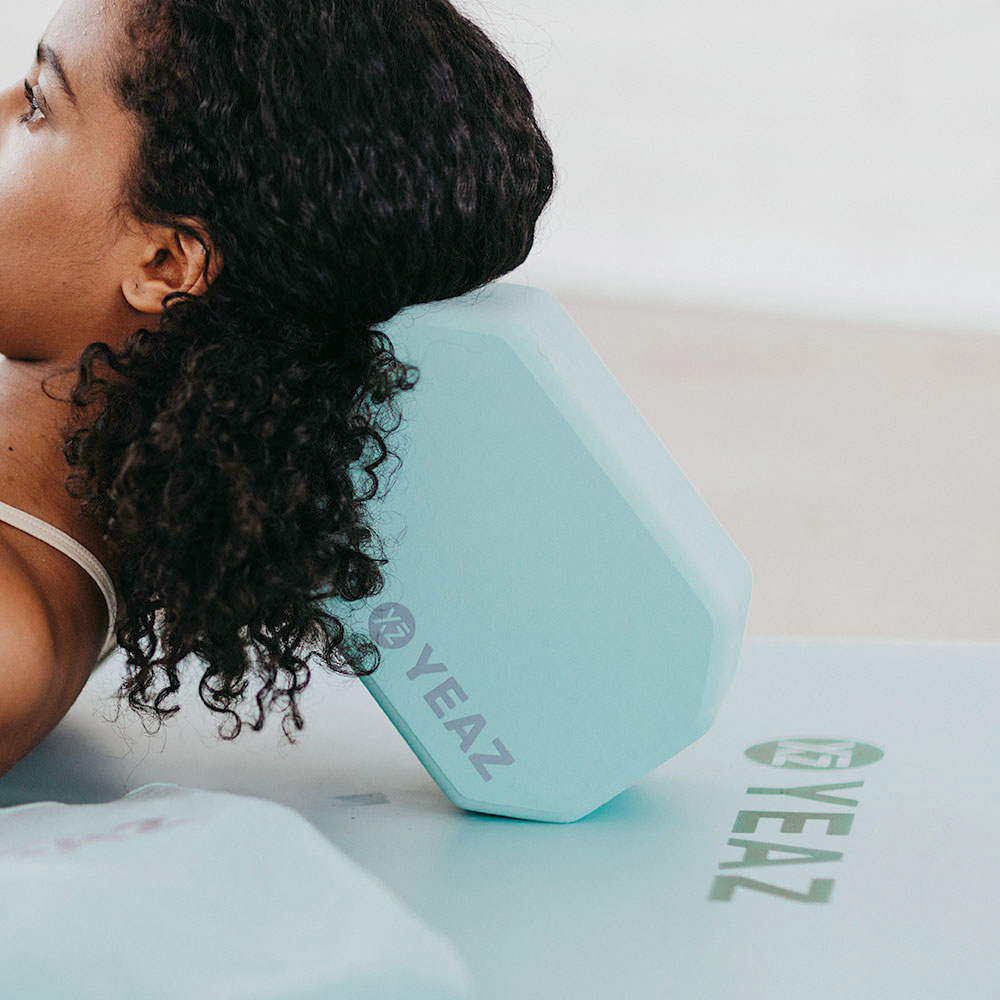 Frau benutzt hellblauen Yogablock. Yogamatte im Hintergrund.
