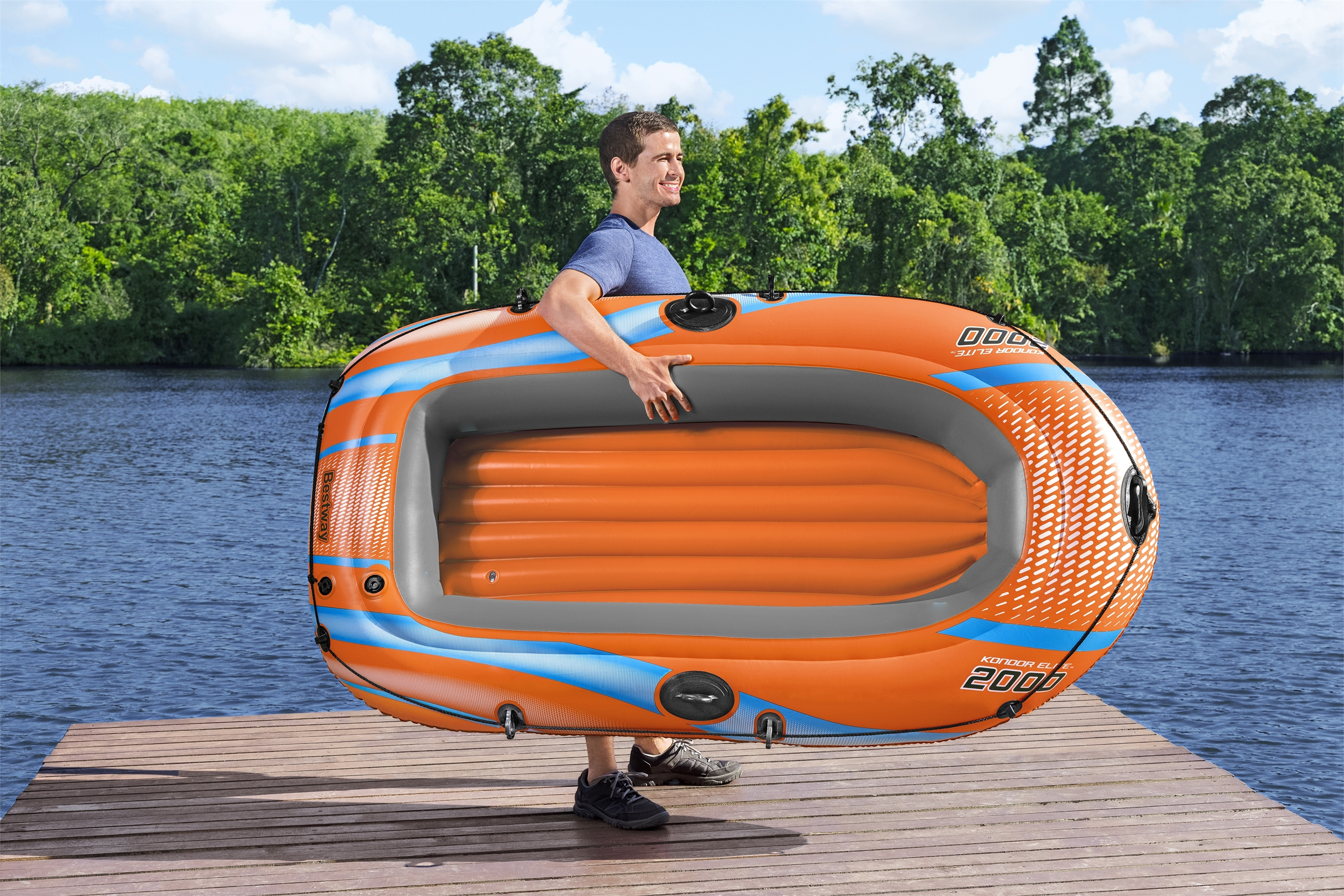 Mann hält ein orangefarbenes Schlauchboot auf einem Steg mit See und Bäumen im Hintergrund.