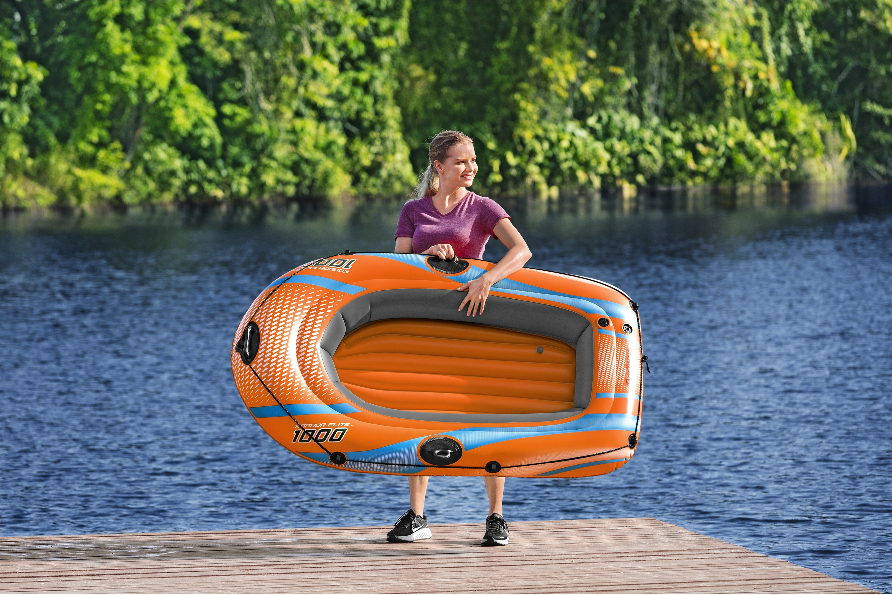 Frau hält ein oranges Schlauchboot auf einem Steg. Wasser und Bäume im Hintergrund, sonniger Tag.
