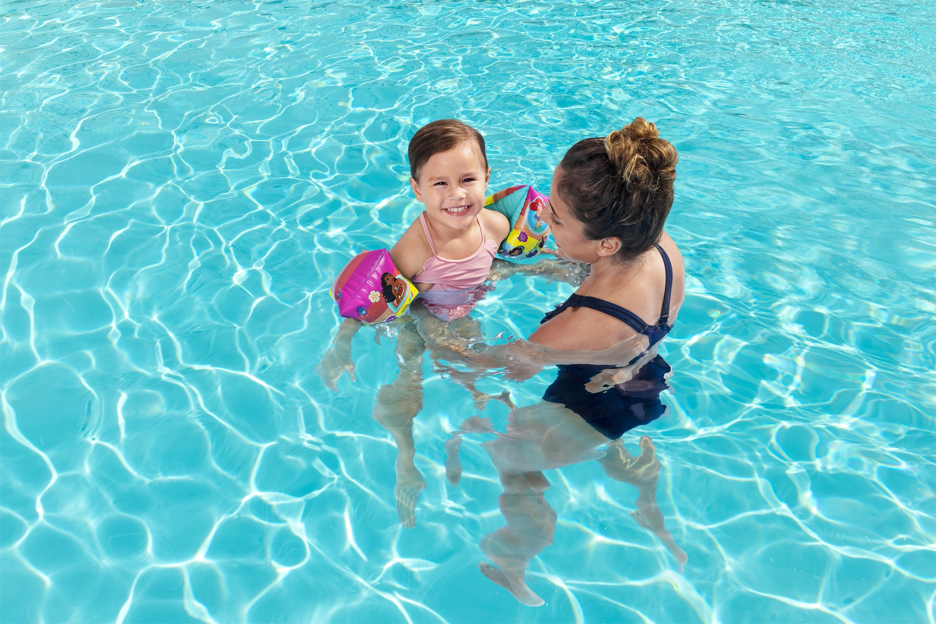 Una mujer y un niño en una piscina. El niño lleva brazaletes y sonríe.