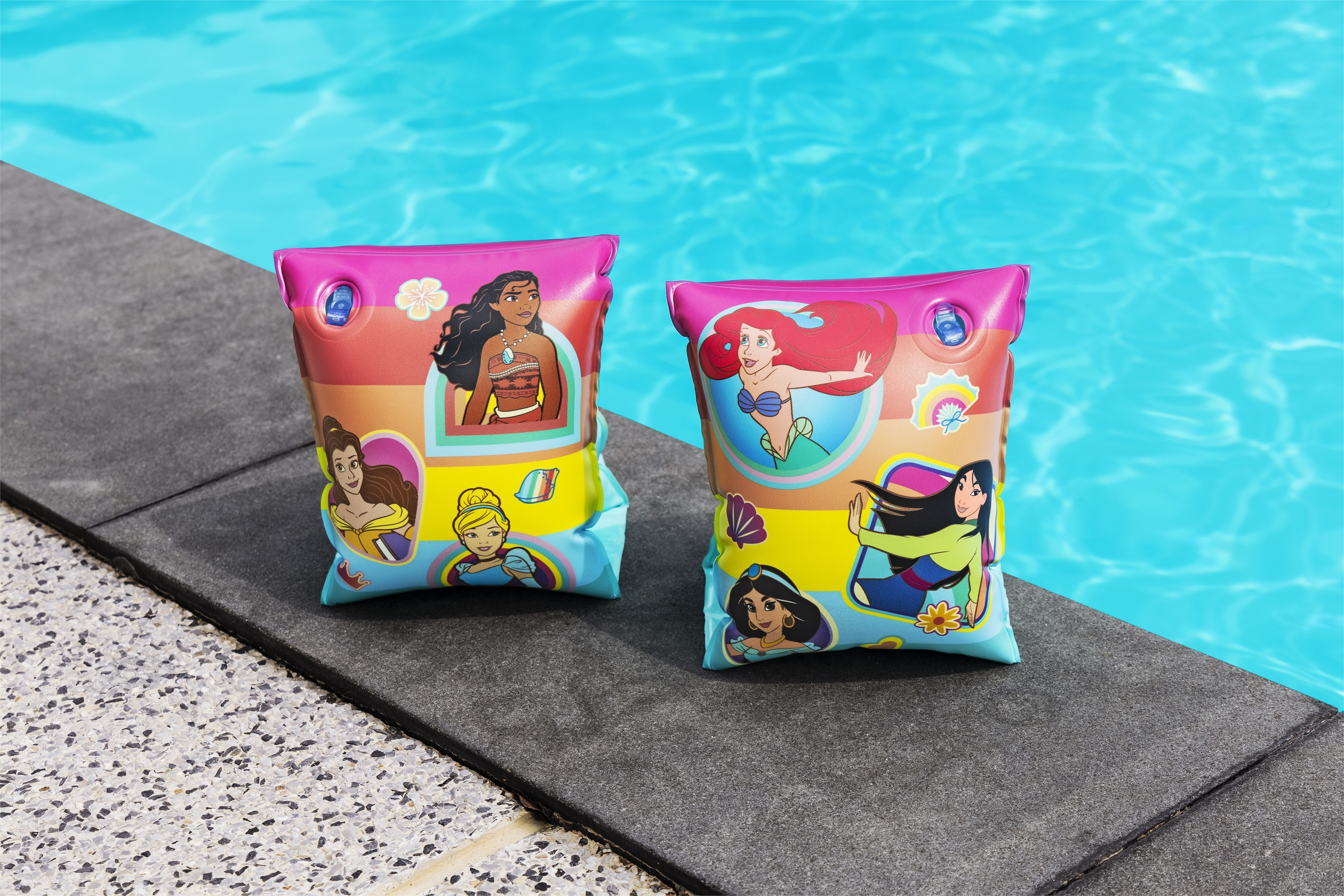 Dos flotadores de brazo rosas y azules con diseños de princesas Disney junto a una piscina.