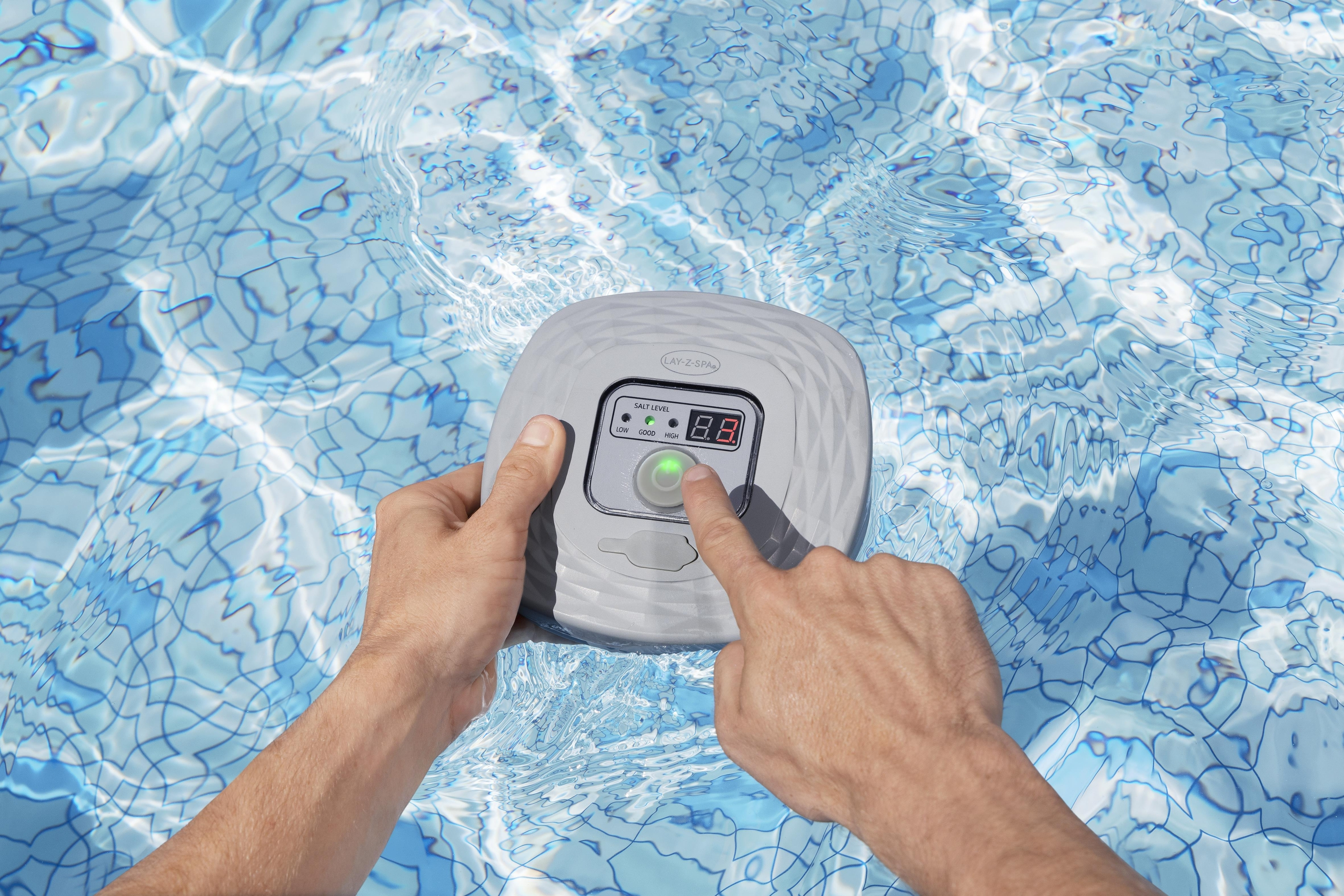 Mani che premono il dispositivo del pannello di controllo Lay-Z-Spa nell'acqua della piscina. Piscina con piastrelle blu.